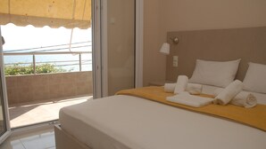 Ein Hotelzimmer mit Bett, Nachttisch, Lampe und Meerblick durch eine Schiebetür.