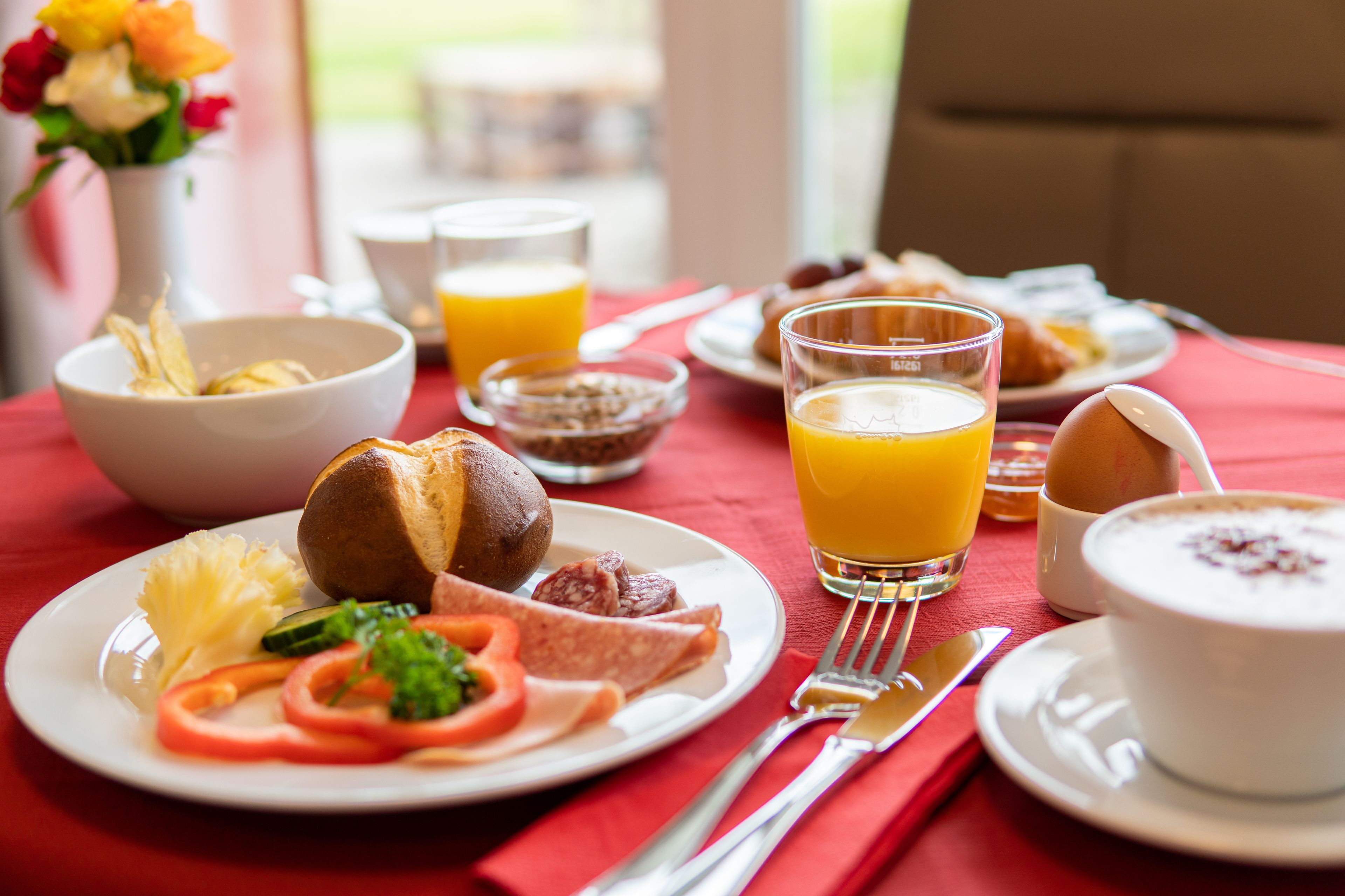 A breakfast table with plates of food, a glass of orange juice, and a bowl of cereal.