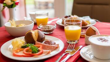 A breakfast table with plates of food, a glass of orange juice, and a bowl of cereal.