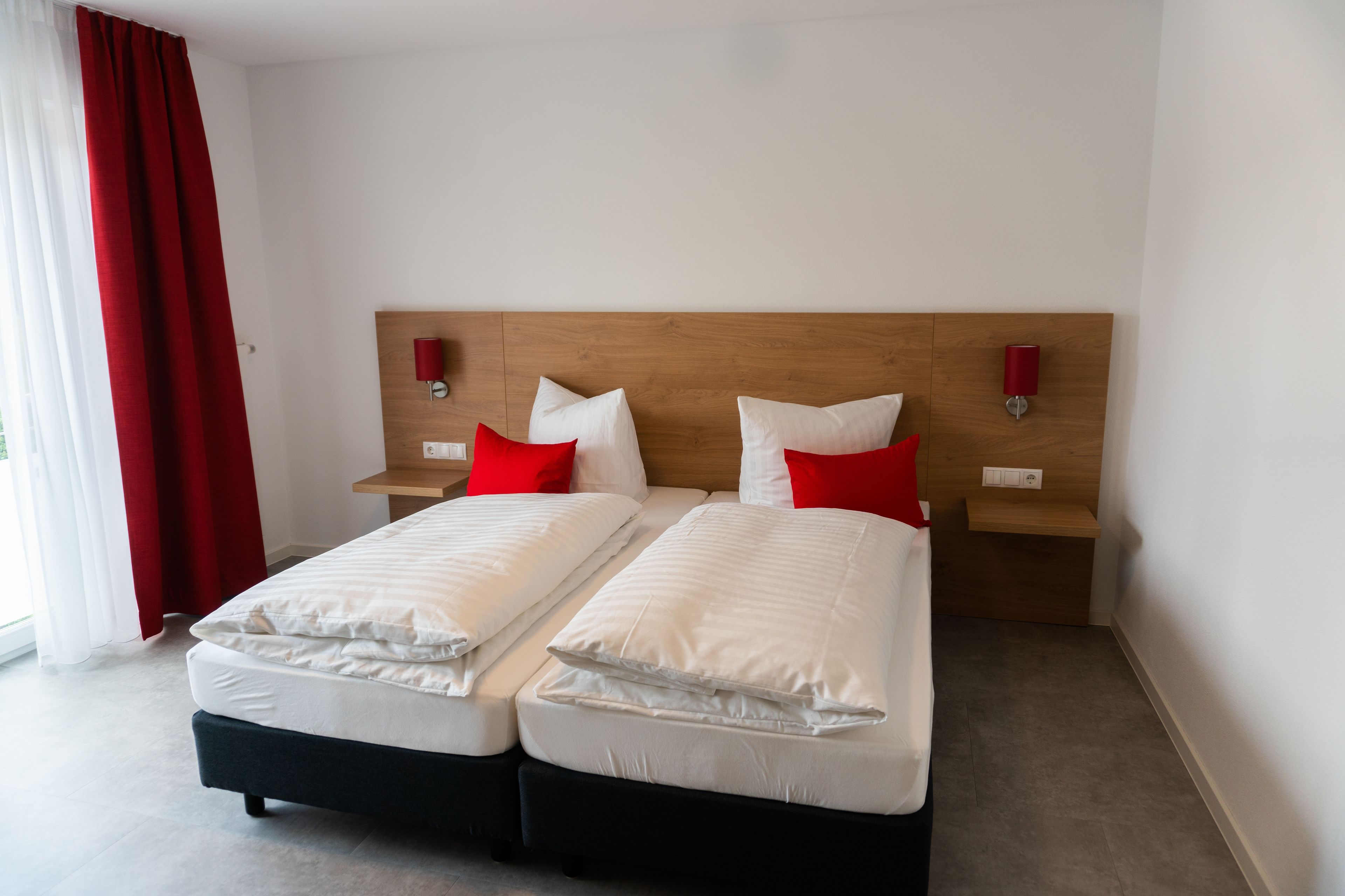 Un lit double avec une literie blanche et des oreillers rouges, deux tables de chevet avec des lampes rouges et une tête de lit en bois.