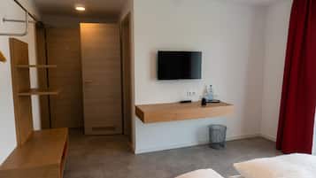 Habitación de hotel con escritorio de madera, televisor montado, pequeño cubo de basura y cortina roja.