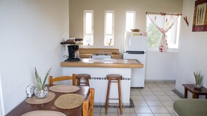 A compact kitchen with a dining area, a refrigerator, and a window with curtains. - Canto del Mar Hotel & Villas (Zihuatanejo)