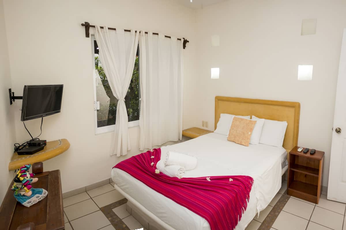 A hotel room with a bed, a TV mounted on the wall, a wooden nightstand, and a door.