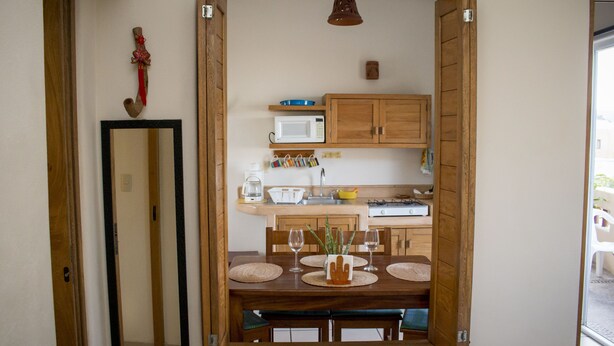 A dining area with a wooden table set for four, a mirror on the wall, and a kitchen in the background. - Canto del Mar Hotel & Villas (Zihuatanejo)