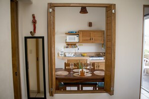 A dining area with a wooden table set for four, a mirror on the wall, and a kitchen in the background. - Canto del Mar Hotel & Villas (Zihuatanejo)
