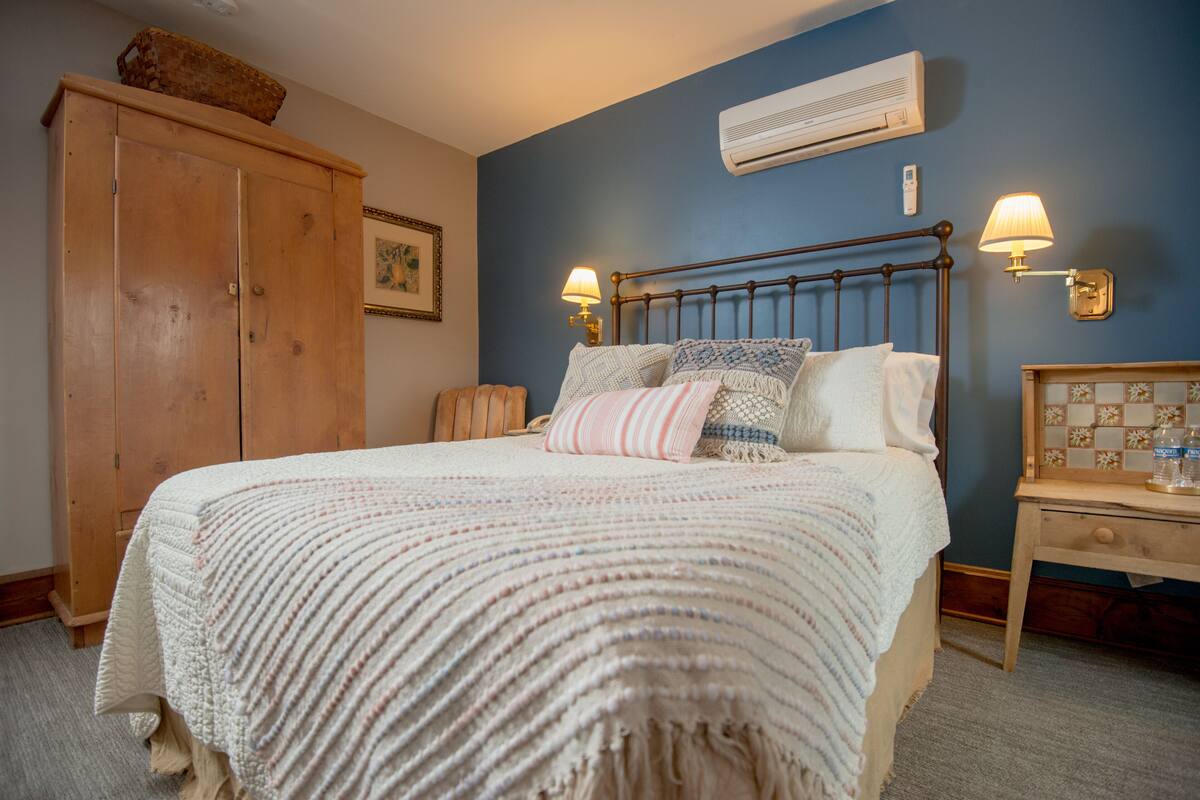 A bedroom with a large bed, wooden wardrobe, bedside lamps, and an air conditioner on the wall.