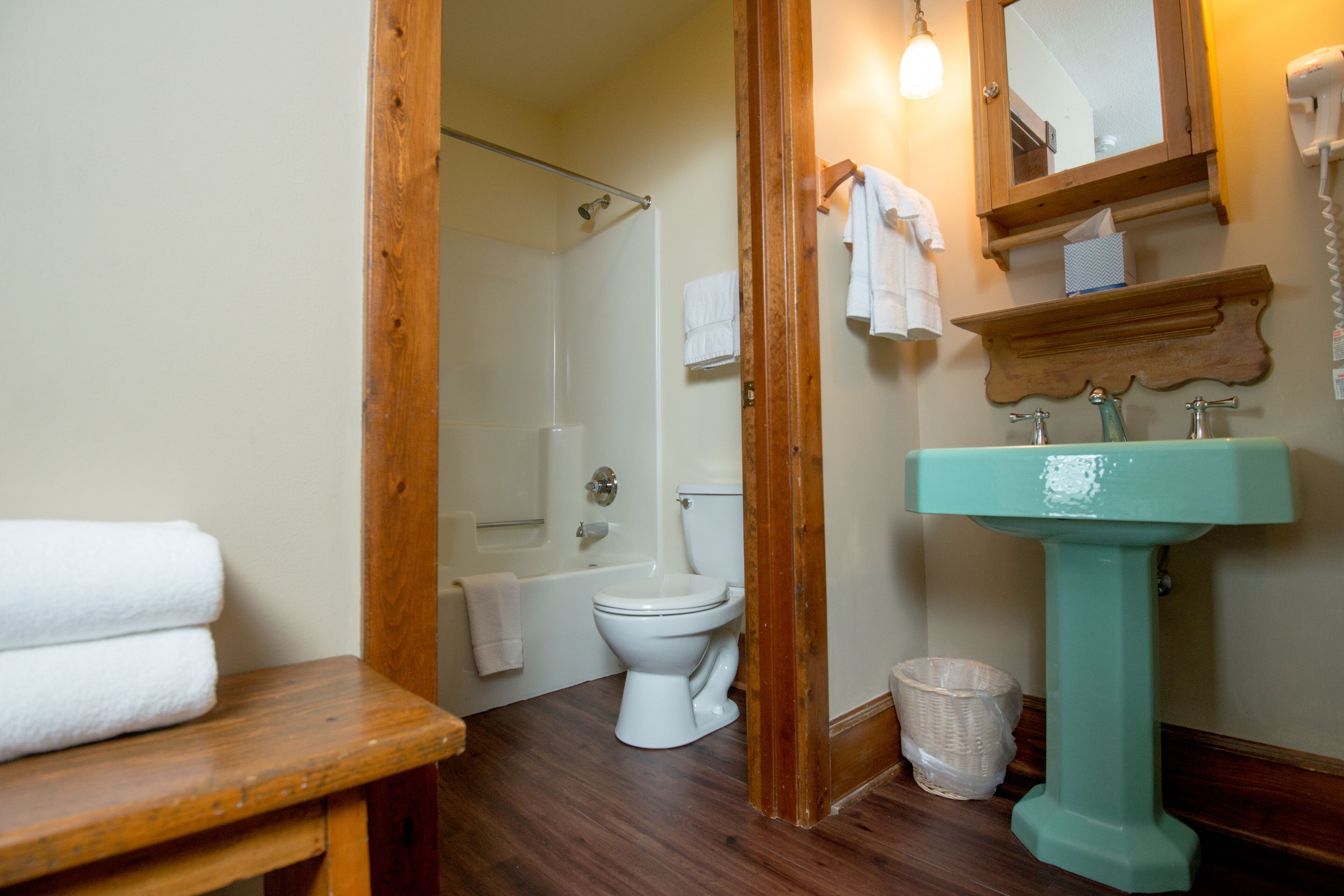 A bathroom with a white toilet, a sink, a bathtub, and a wooden bench.