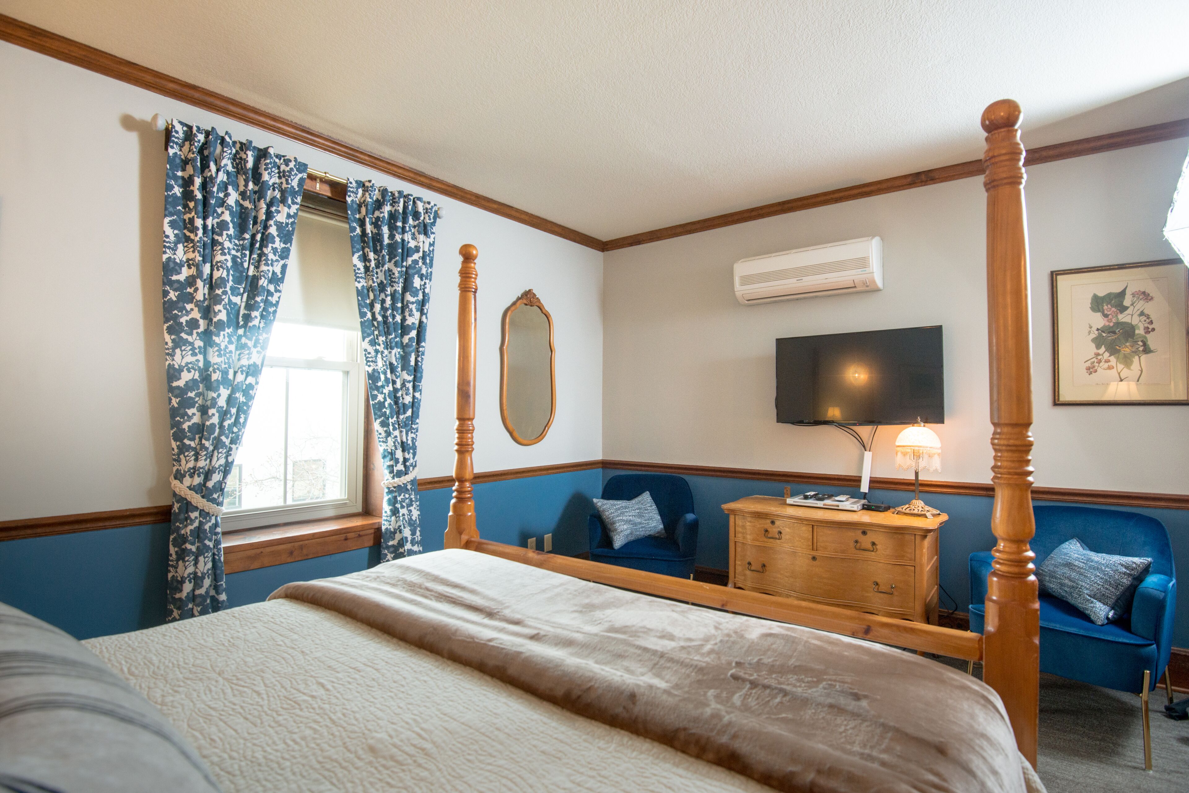 A bedroom with a four-poster bed, a dresser, a chair, a mirror, and a television.