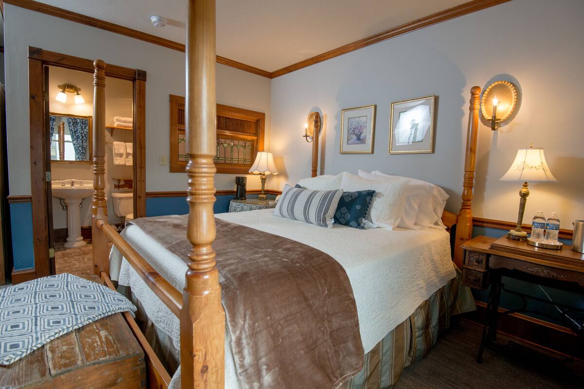 A bedroom with a four-poster bed, a wooden nightstand, a dresser, and a mirror.