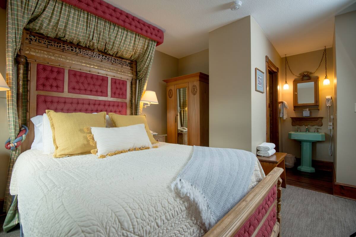 A neatly made bed with a quilted headboard, a wooden nightstand with a lamp, and a wooden wardrobe.