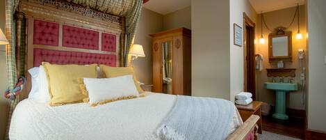 A neatly made bed with a quilted headboard, a wooden nightstand with a lamp, and a wooden wardrobe.