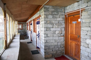 Corredor com paredes de pedra, portas de madeira e um sinal indicando um banheiro.