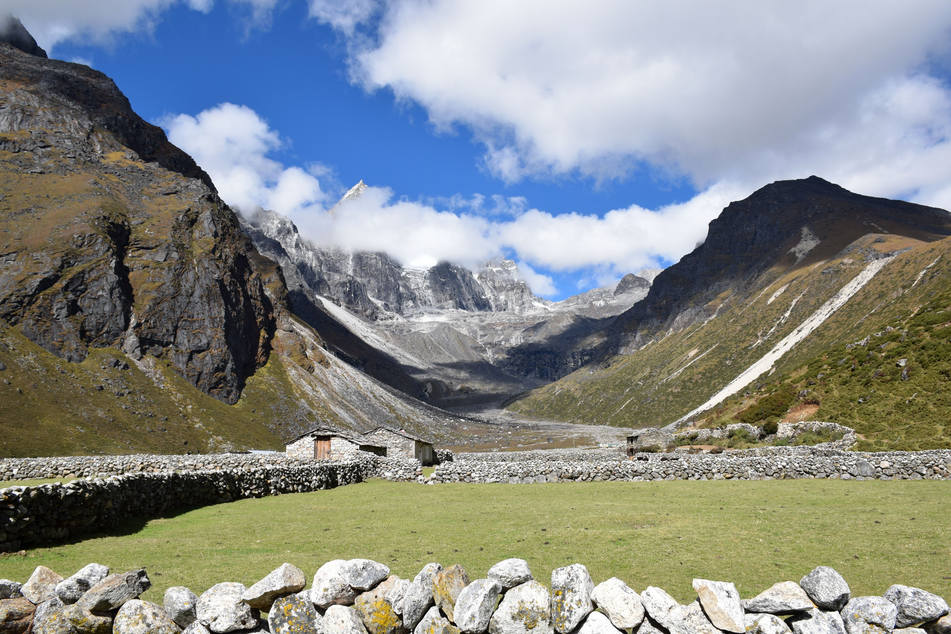 A stone wall with a small building in a mountainous area.