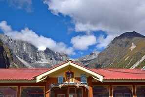 Een berghut met een rood dak en traditionele architectuur, gelegen voor een achtergrond van ruige bergen en een helderblauwe lucht.