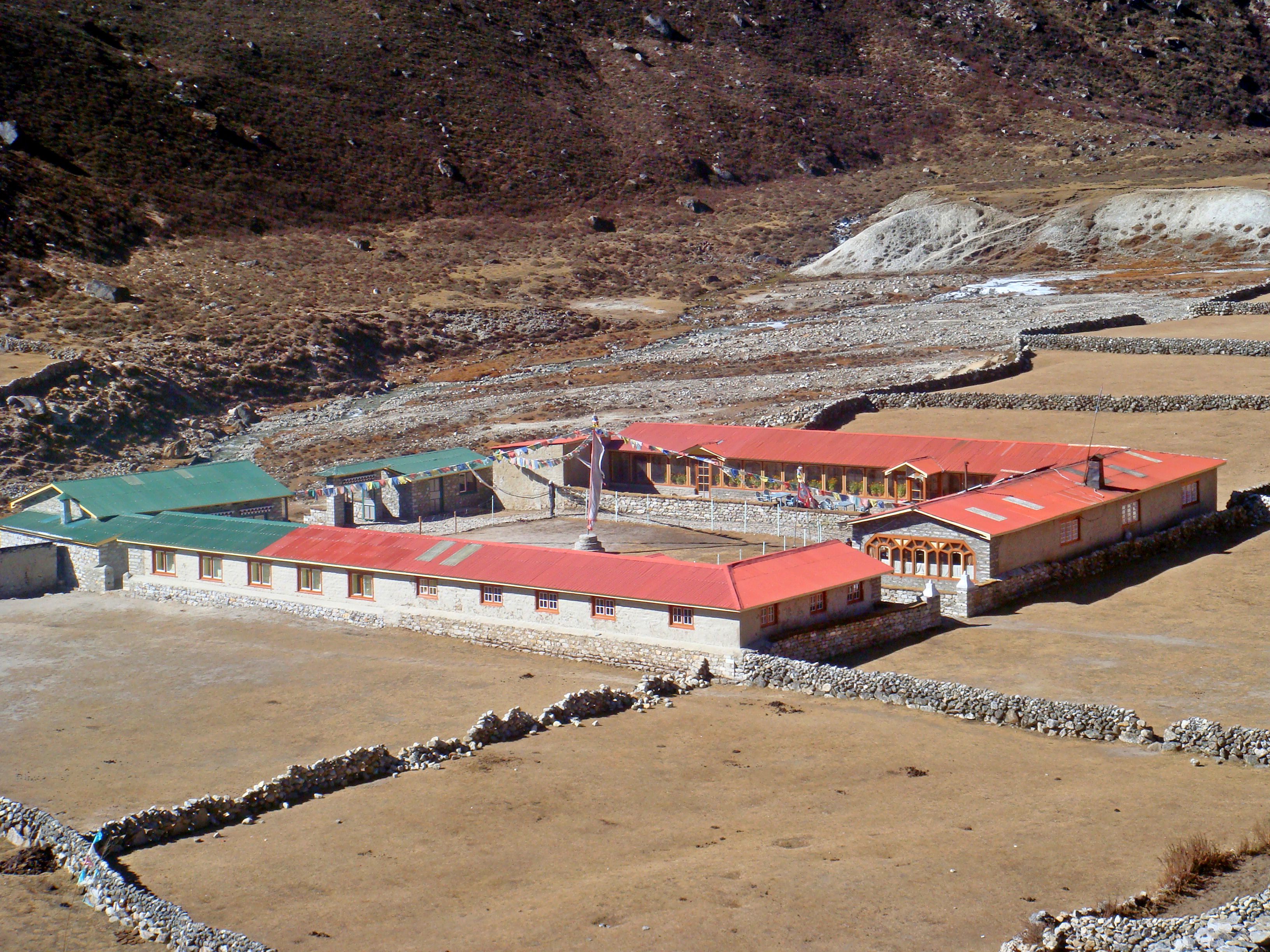 Un edificio de techo rojo y paredes de piedra, rodeado por un paisaje rocoso.