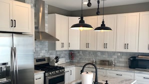 A modern kitchen with white cabinets, stainless steel appliances, a marble island, and blue bar stools.