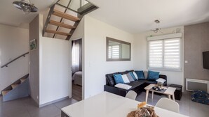 A modern living room with a staircase, a sofa set, a dining table, and a large window with blinds. - Ocean guardians' house with spa,  (Plougonvelin)