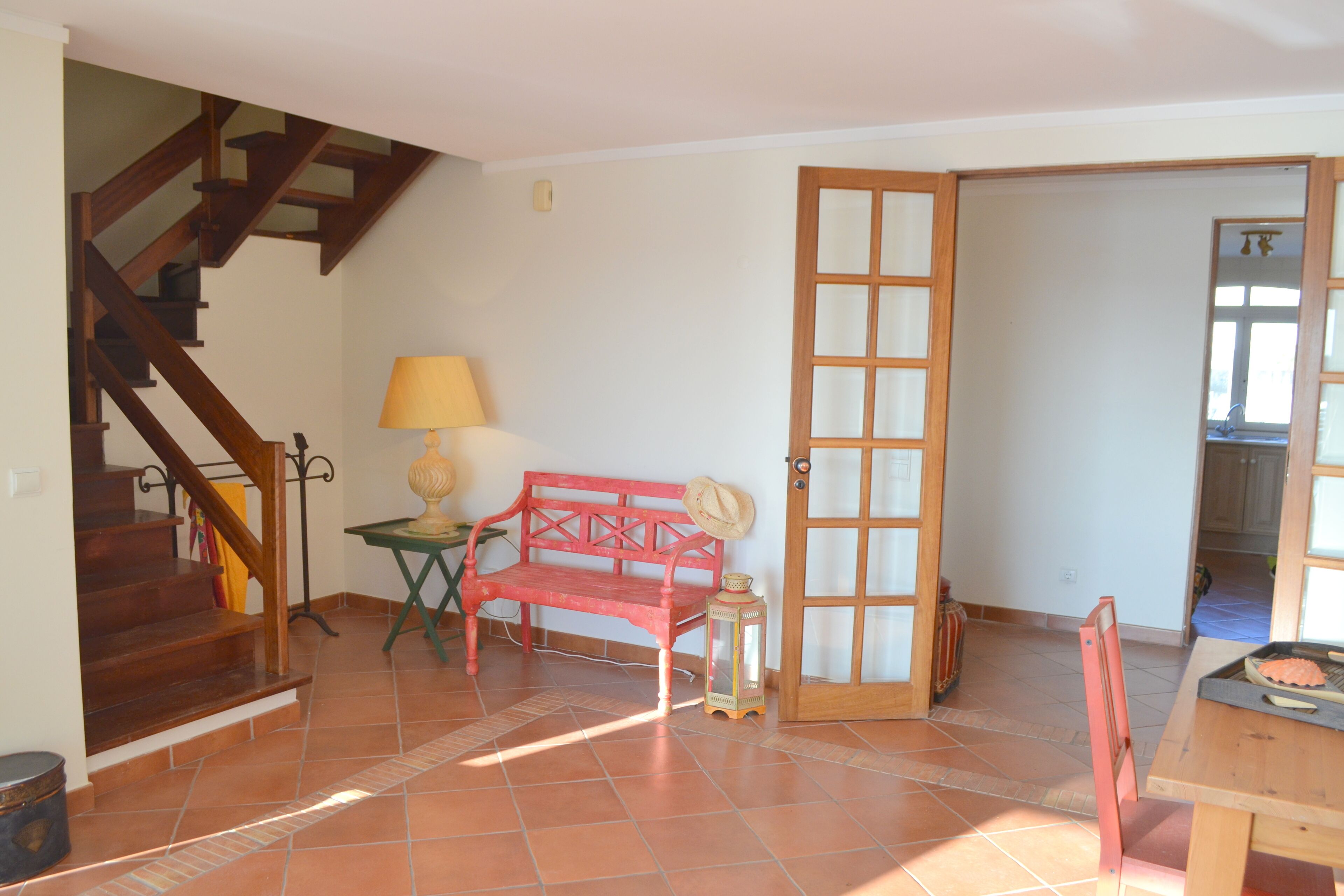 A room with a wooden staircase, a red bench, a table with a grill, and a door leading to another room.
