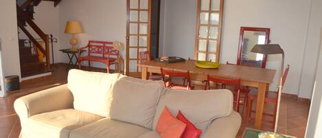 A living room with a sofa, a dining table, chairs, a lamp, and a mirror.