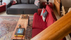 Ein Wohnzimmer mit grauem Sofa, rotem Sessel und einem Holztisch. An der Wand befinden sich abstrakte Gemälde und ein Holzschrank.