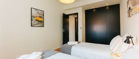 Une chambre d’hôtel avec deux lits, une grande armoire sombre et une image encadrée accrochée au mur, ainsi qu’une lampe suspendue.