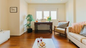 A living room with a wooden floor, a white sofa, a dining table with chairs, and a potted plant. - RENT4REST LISBON FAMILY & FRIENDS APARTMENT IN ROMA AVENUE (Lisboa ciudad)