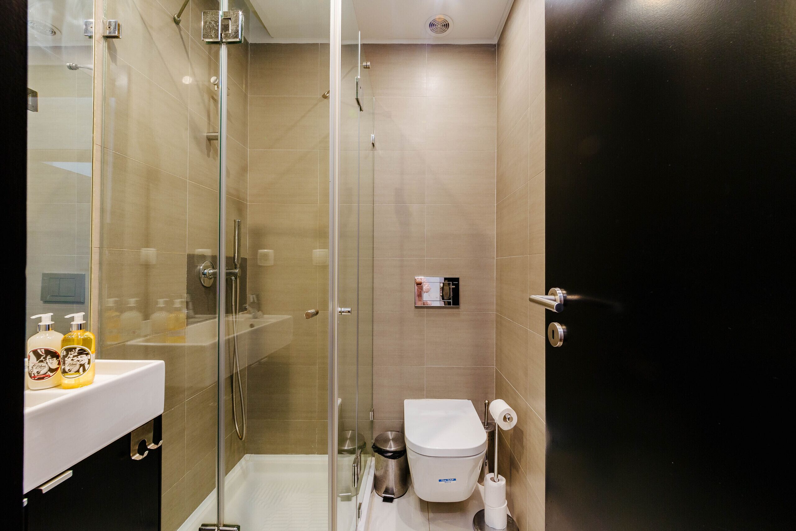 Un bagno moderno con doccia vetrata, un lavandino bianco con articoli da toilette e un water con portaserviti di carta.