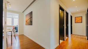 A hallway with wooden flooring, white walls, and doors leading to other rooms. There is a table with chairs and a painting on the wall. - RENT4REST LISBON FAMILY & FRIENDS APARTMENT IN ROMA AVENUE (Lisboa ciudad)