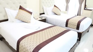 A hotel room with two beds, each with a tufted headboard, white bedding, and brown decorative pillows. - Gondar Plaza Hotel (Gondar)
