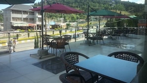 An outdoor seating area with tables and chairs, umbrellas, and a view of a hilly landscape in the background. - Gondar Plaza Hotel (Gondar)