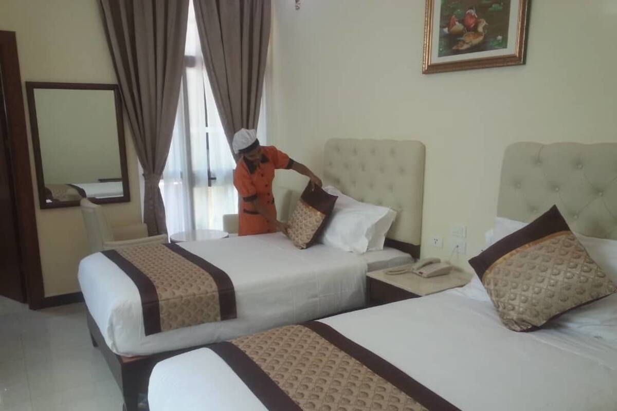 A hotel room with two beds, each with a patterned bedspread and pillows, a bedside table with a telephone, and a mirror on the wall.