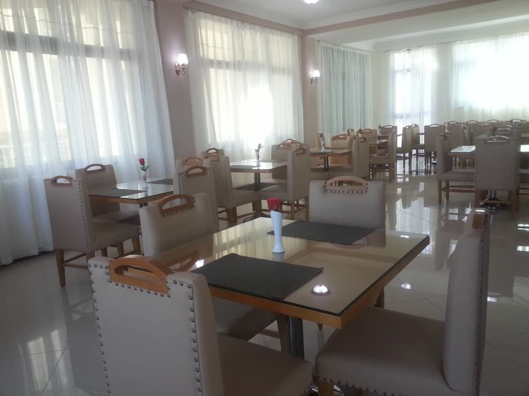 A spacious dining area with multiple tables and chairs, large windows with sheer curtains, and a clean, modern design.