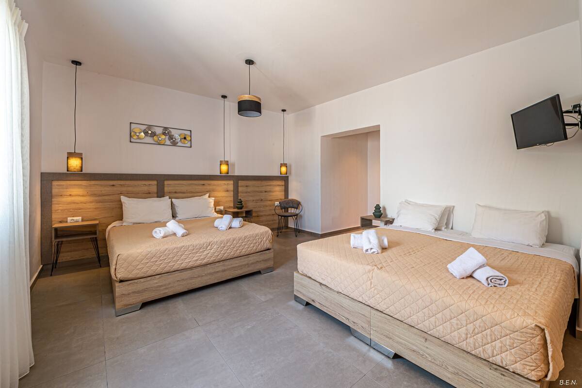 A hotel room with two beds, a wooden headboard, a flat-screen TV mounted on the wall, and a small table with a chair.