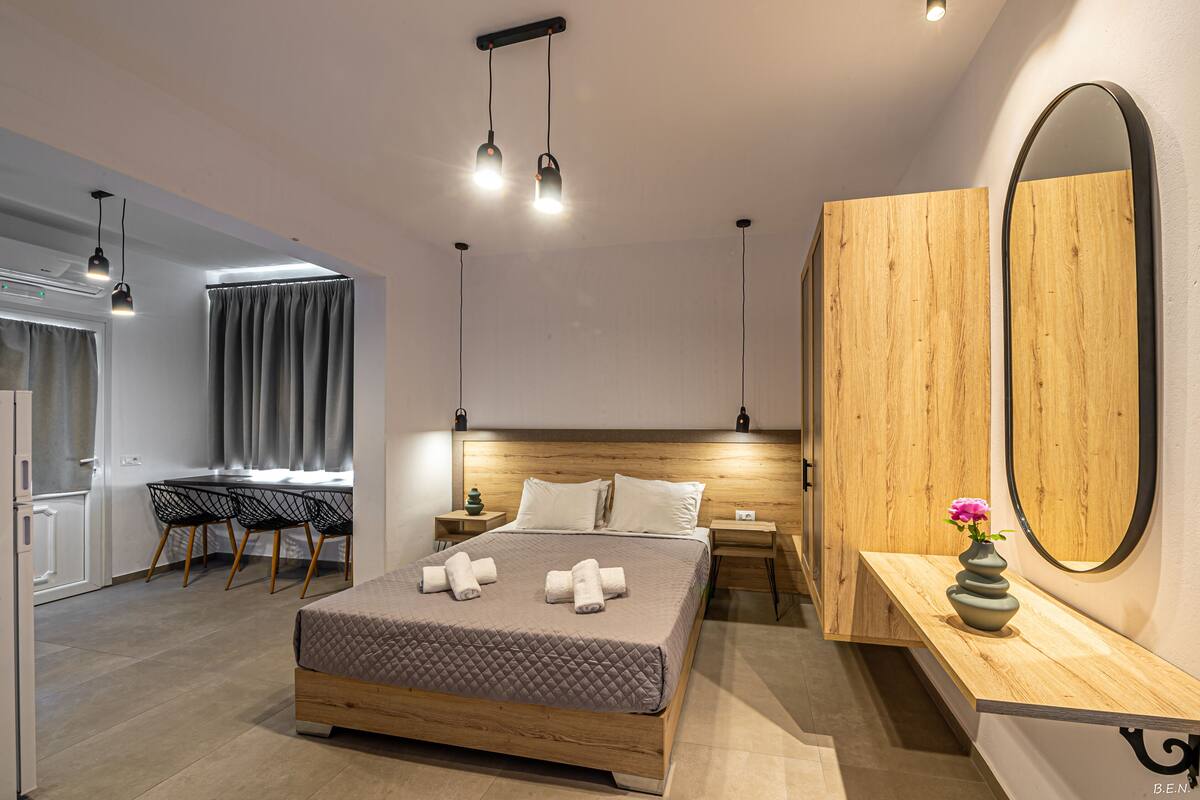 A modern bedroom with a wooden bed, bedside tables, a large mirror, and a desk with chairs.