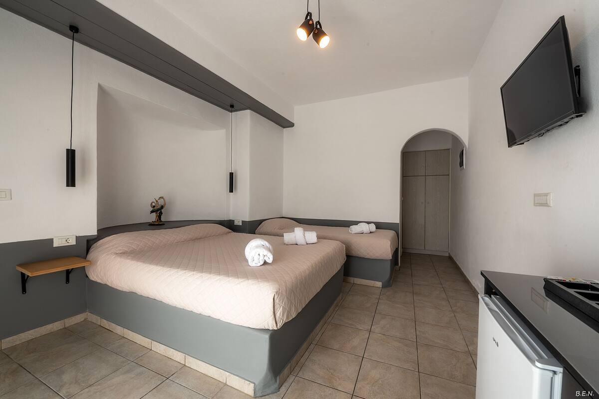 A modern hotel room with a large bed, a small bedside table, a flat-screen TV, and a built-in bench.