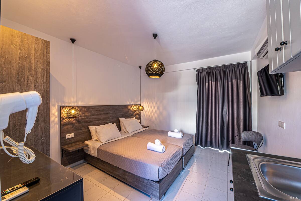 A modern hotel room with a large bed, bedside lamps, a hairdryer, a remote control, a sink, and a chair.