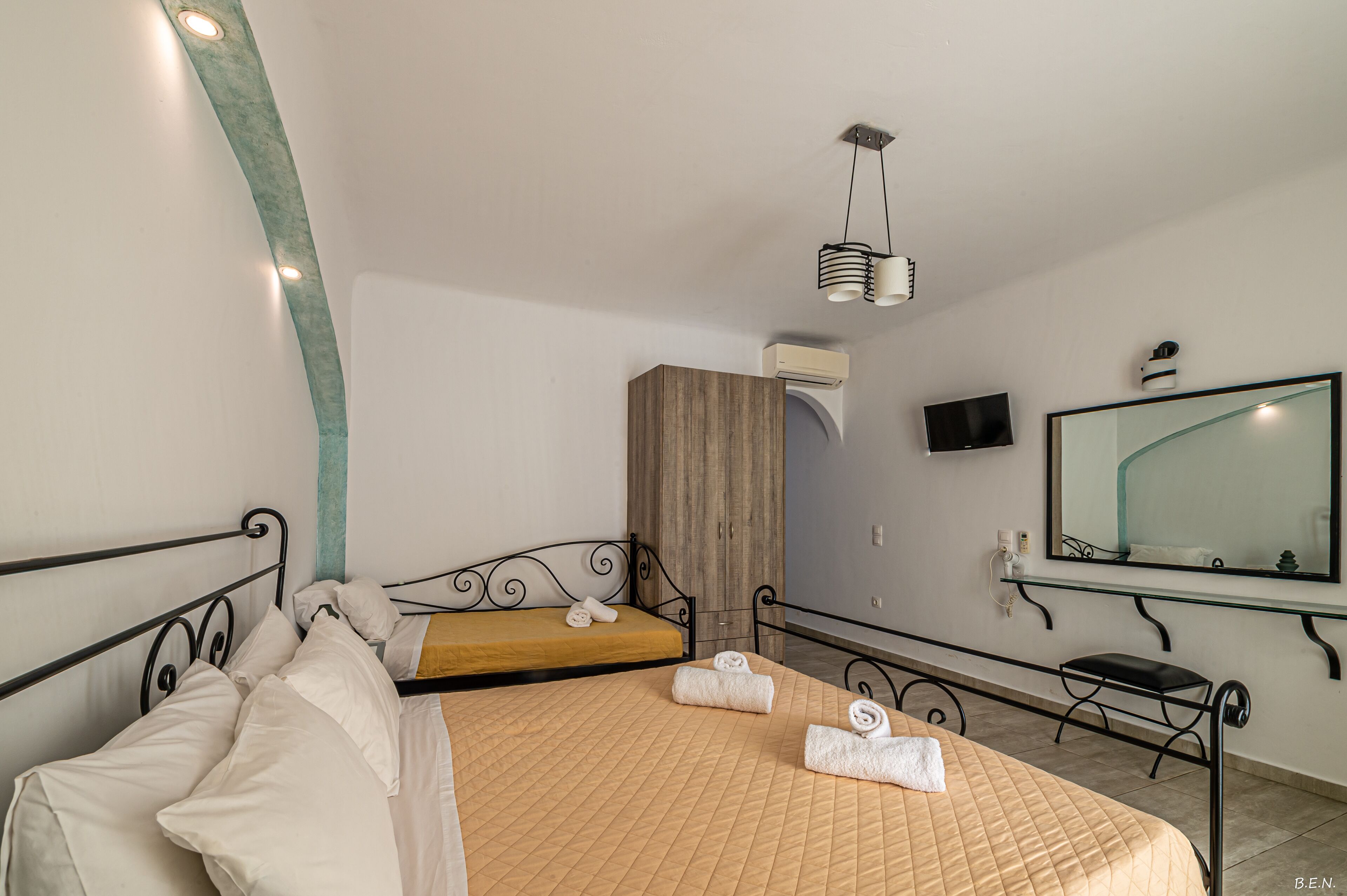 A hotel room with a bed, a wooden wardrobe, a television, a mirror, and a ceiling light fixture.