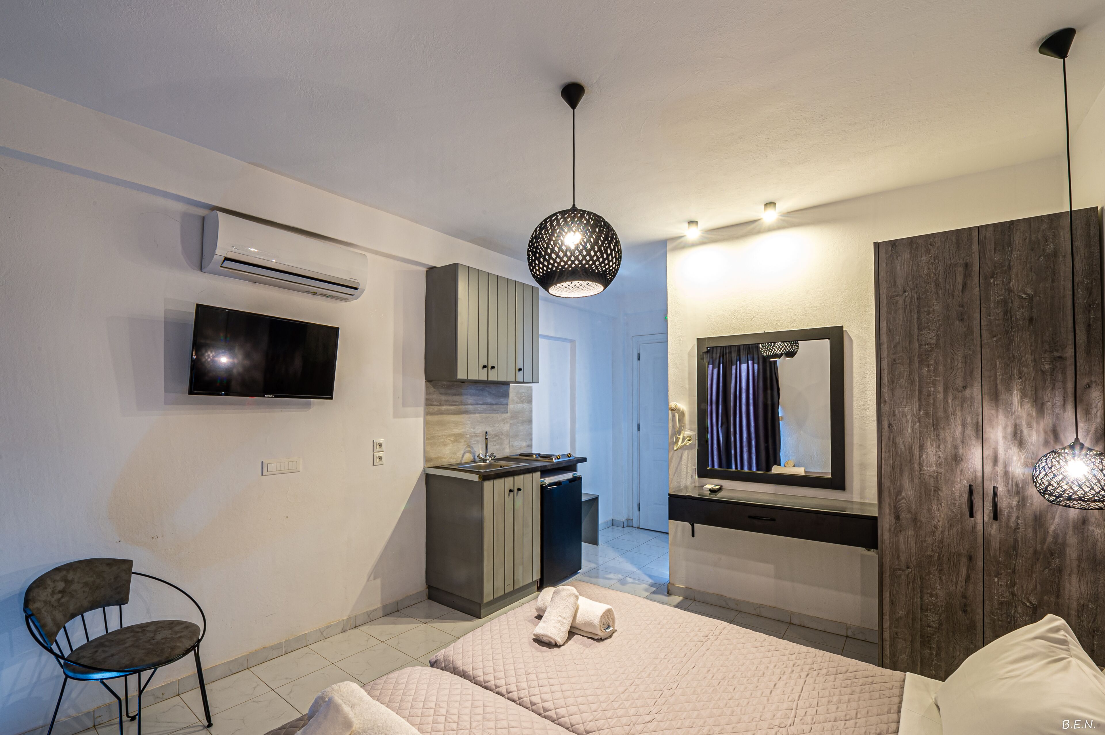 Une chambre d’hôtel moderne équipée d’un lit, d’une petite kitchenette, d’un téléviseur fixé au mur et d’une armoire en bois.