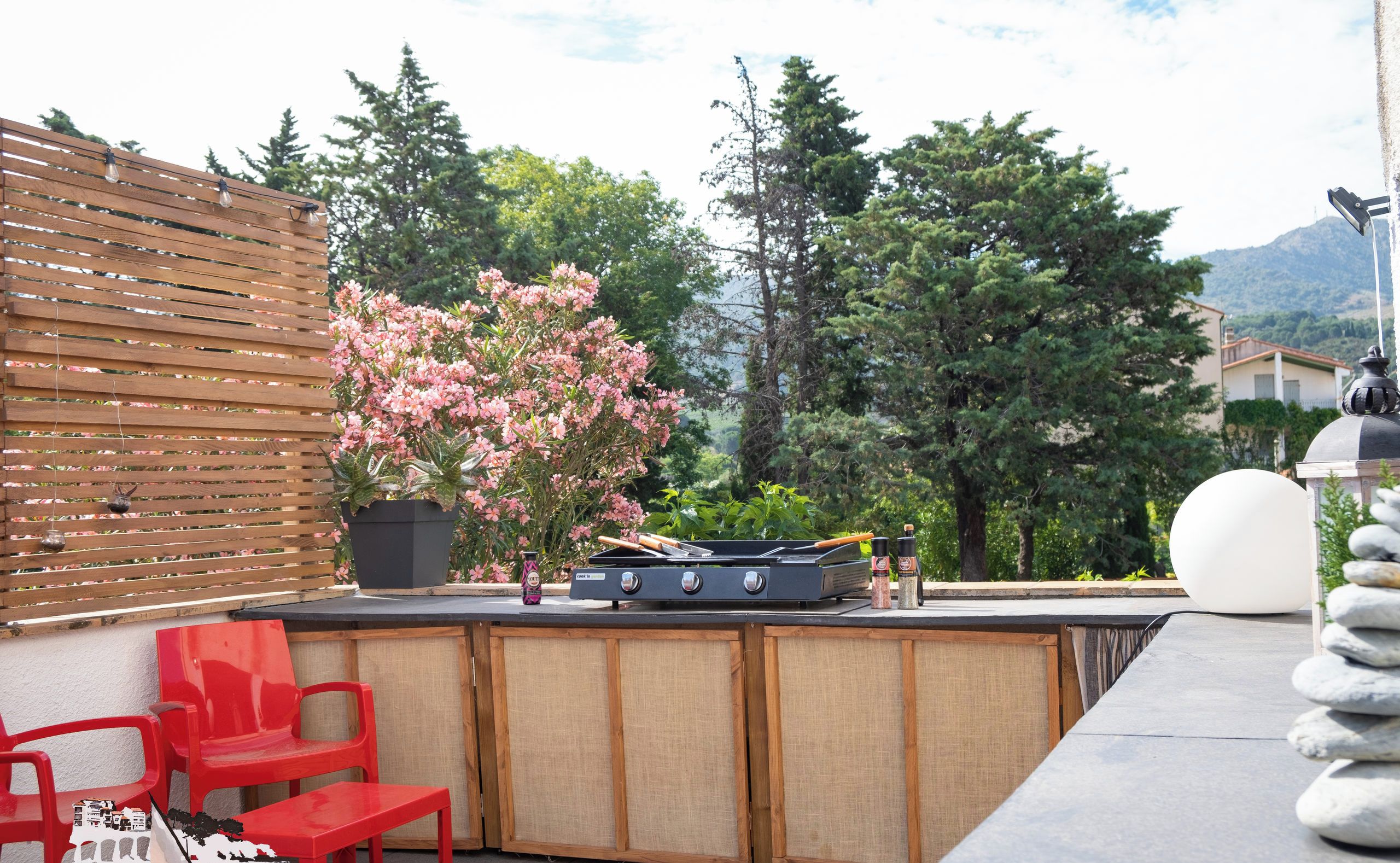 Un patio al aire libre con una parrilla, sillas rojas y una cerca de madera.