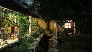 Une cour faiblement éclairée, avec un chemin de pierre menant à un bâtiment doté d’une porte en bois.