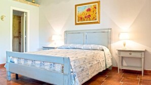 Une chambre à coucher comprenant un lit, deux tables de chevet, une commode, une porte et un tableau accroché au mur.