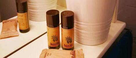 Un estante en el baño con dos plantas en macetas, dos botellas de jabón Dolce Azzura y una pastilla de jabón.