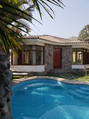A house with a stone facade, a swimming pool, and a stone wall.
