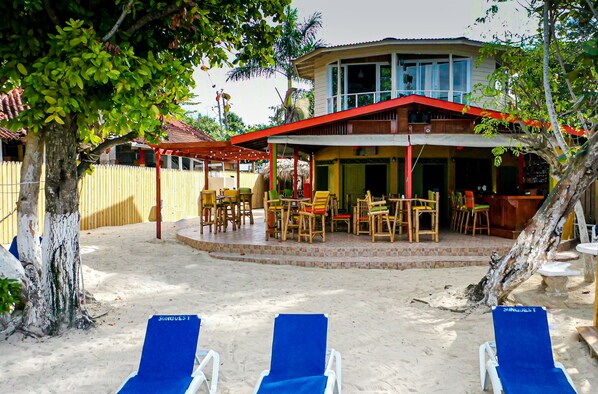 Un resort frente al mar con un área de comedor cubierta, asientos al aire libre y sillones de descanso.