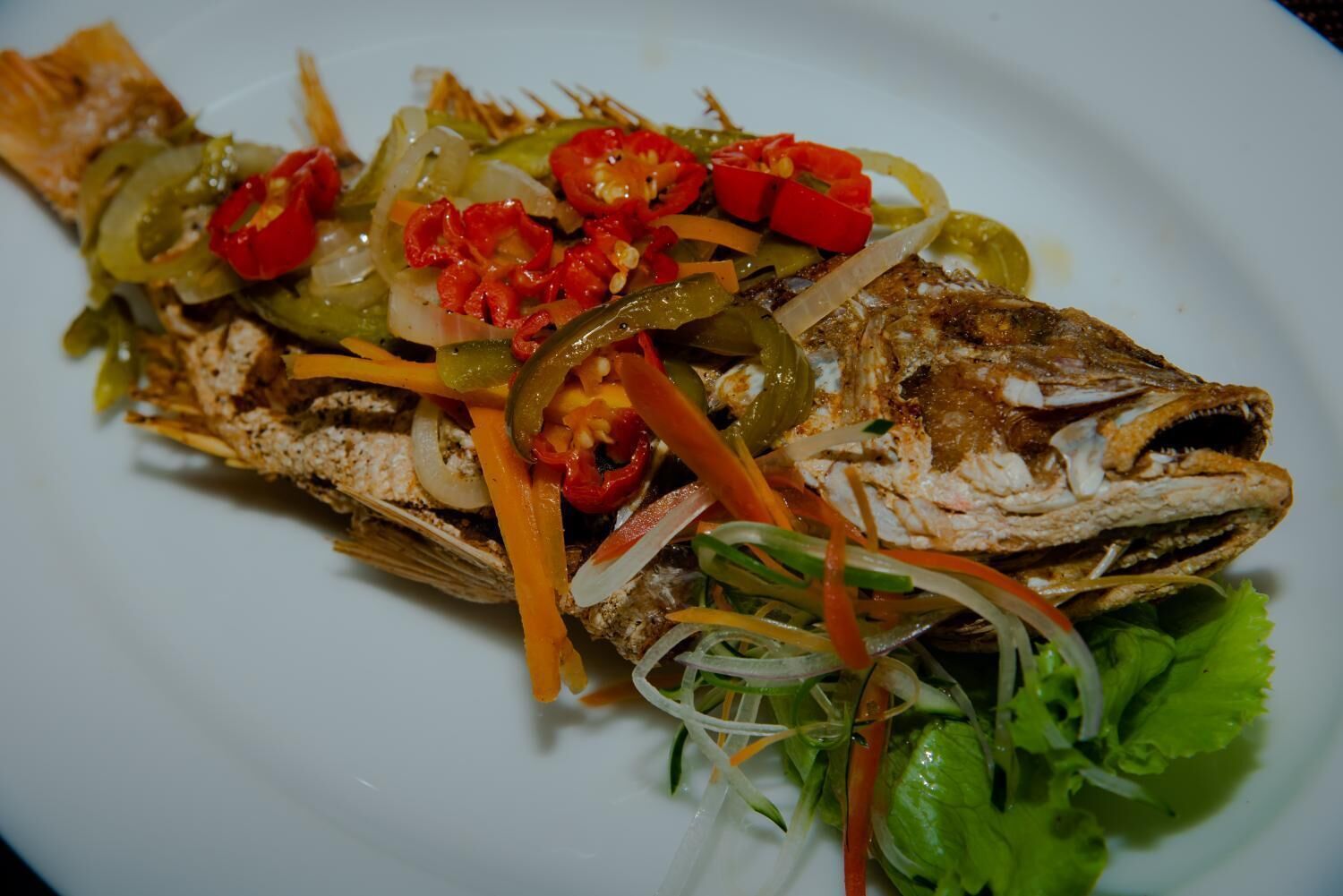 A grilled fish dish with vegetables on a white plate.
