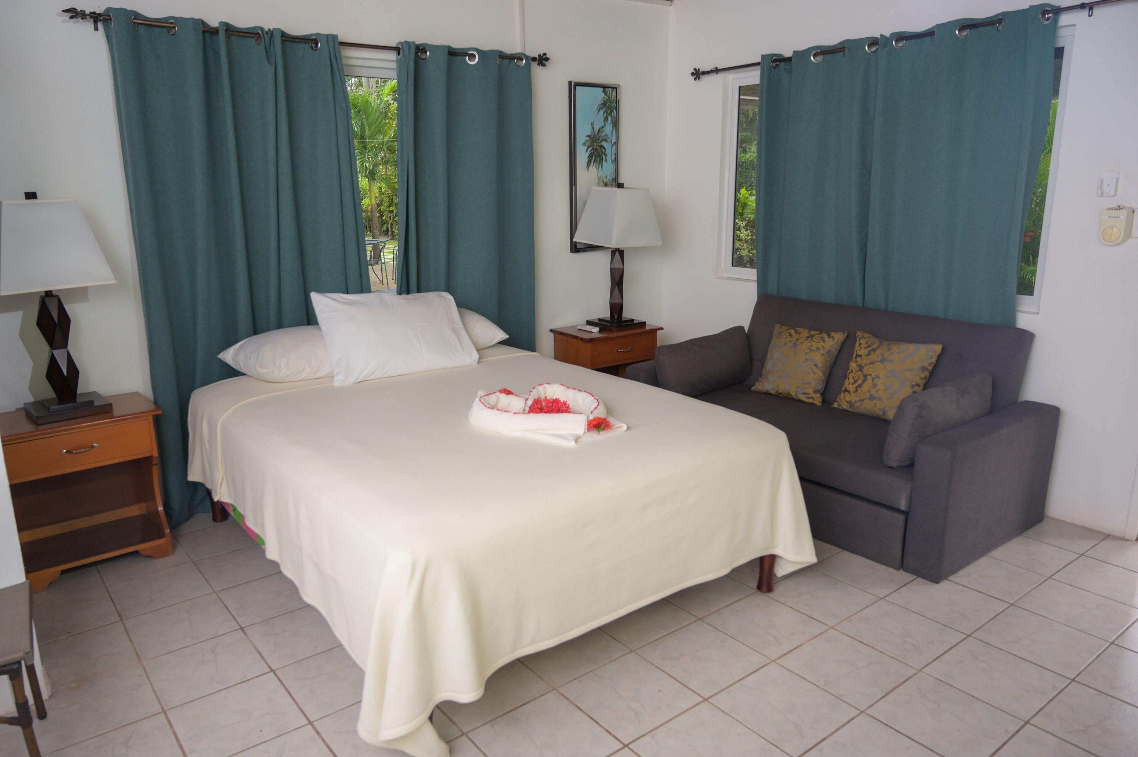 Un dormitorio con cama, mesita de noche, lámpara de pie, sofá y ventana con cortinas.