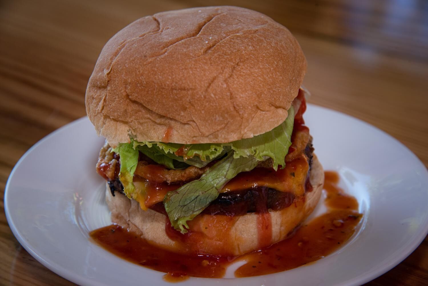 Un hamburger avec de la laitue, du fromage et un pain, servi sur une assiette blanche.