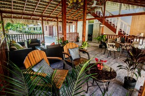 A covered outdoor seating area with wooden furniture, potted plants, and a staircase leading to an upper level. - Xye   Resort (Negril)