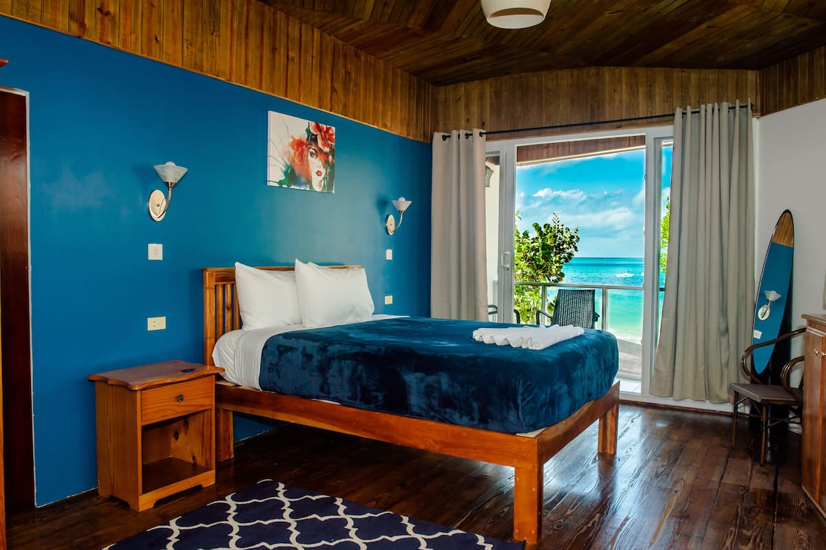Un dormitorio con cama de madera, mesita de noche, pared azul y vista al océano.