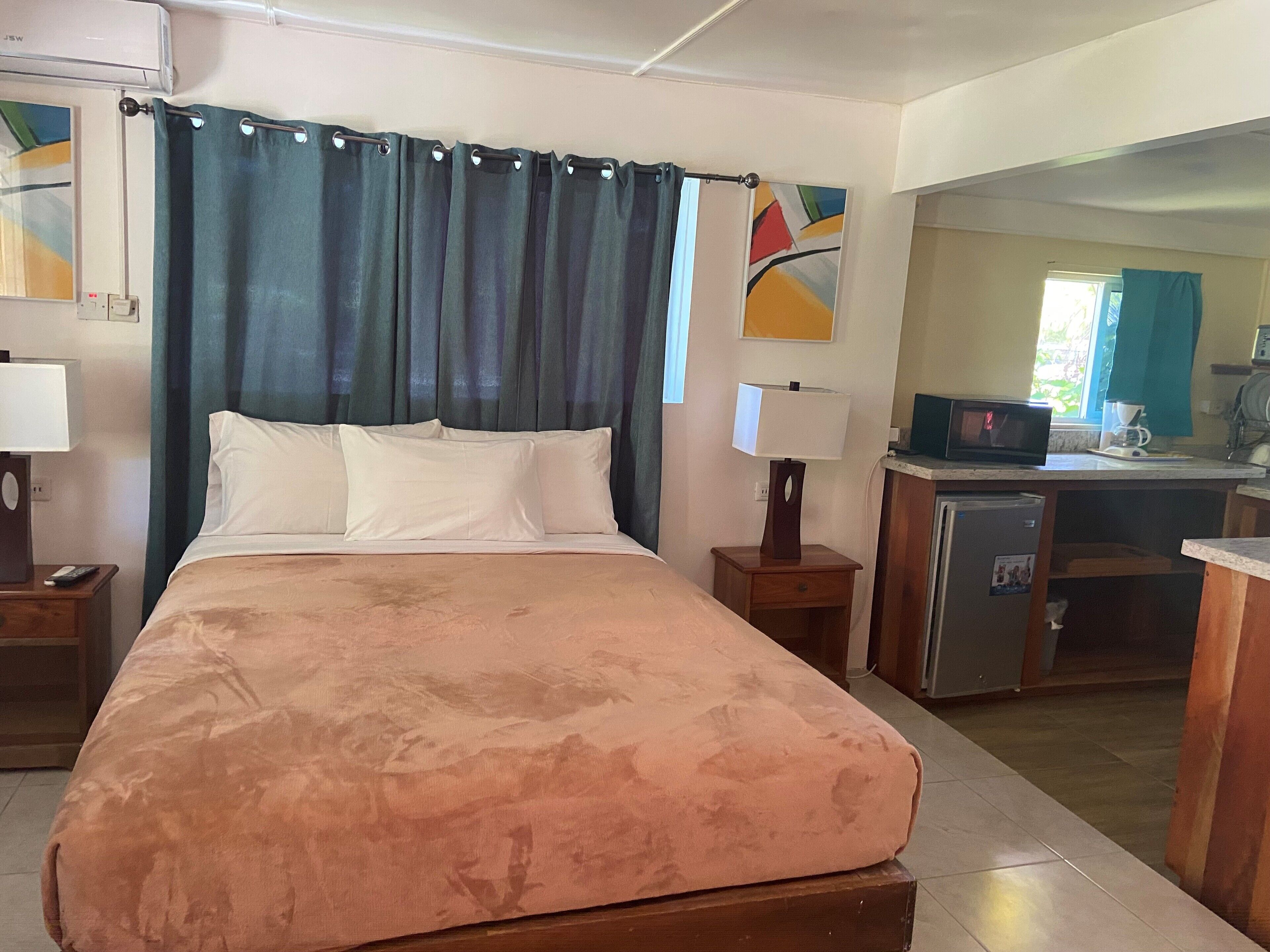 A hotel room with a bed, two bedside tables, a desk with a microwave, and a small kitchenette.